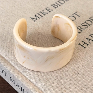 Macro shot of irregular wide acrylic bangle with cream marble texture on a book background