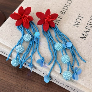 Vibrant red flower drop earrings with blue beaded tassels on a vintage art book