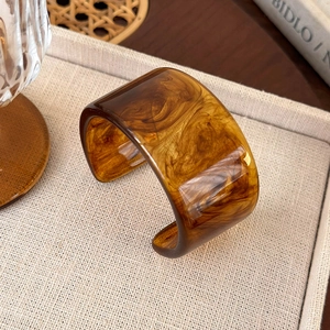 Close-up of amber resin bangle showing marble texture on a textured beige tray