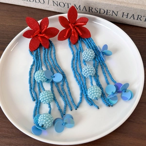 Macro detail of red felt flower earrings with long blue beaded fringe tassels
