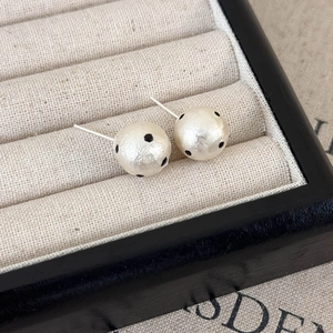 Dettaglio dei orecchini a perno con perle a pois crema in un portagioie beige morbido