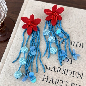 Detailed close-up of long blue beaded tassel earrings with red fabric flowers on beige linen