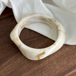 Detail of wide irregular acrylic resin bangle with cream amber marble texture on wood