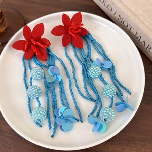 Detailed close-up of long blue beaded tassel earrings with red felt flower petals