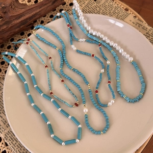 Bohemian pearl and turquoise beaded necklaces layered in a minimalist ceramic dish