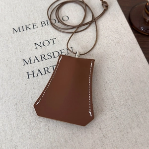 Detail view of brown faux leather key case with white hand-stitching and metal clasp