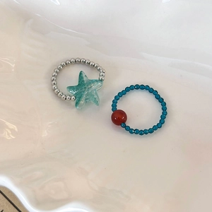 Mint green starfish beaded ring set with silver and blue beads on a white shell plate