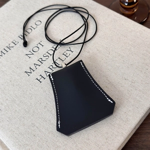 Detail of black leather bell key case pendant with white contrast stitching and neck cord
