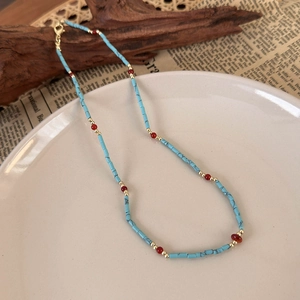 Close-up of blue and red beaded necklace with golden lobster clasp on a ceramic plate