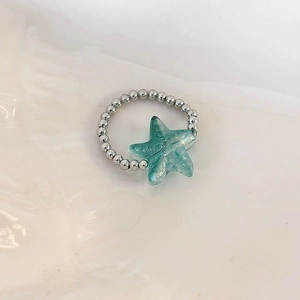 Macro detail of mint green starfish pendant on silver beaded ring with water wave background