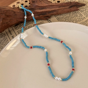 Detailed view of light blue beaded necklace with white pearls and gold spacers on white ceramic