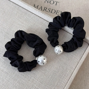 Set of two black polka dot pearl scrunchies on a textured minimalist background