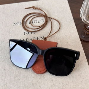 Detail view of black square oversized sunglasses with brown leather case and lanyard