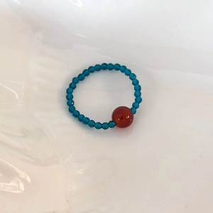 Detail of beaded ring featuring faceted blue beads and a central smooth red agate stone