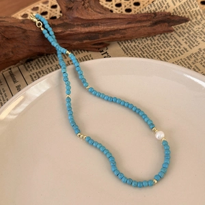 Detail of turquoise beaded necklace with gold spacers and a white pearl on white plate