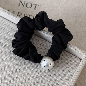 Close-up of a black pleated scrunchie with a polka dot pearl bead on beige linen tray