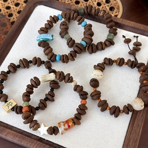 Detail of coffee bean beaded bracelet featuring cat paw and mahjong charms on wood tray