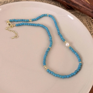 Detail of turquoise beaded necklace with white pearl and gold hardware on a tray