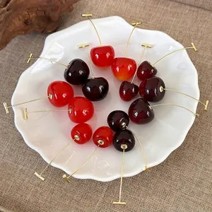 Red and purple cherry earrings with golden stems arranged in a white shell dish