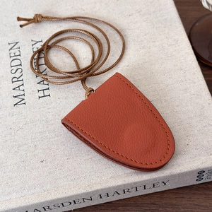 Detail of orange lychee grain leather hat clip with precise stitching and adjustable brown lanyard