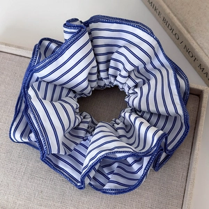 Détail de l'élastique à cheveux géant en tissu rayé bleu posé sur un plateau neutre