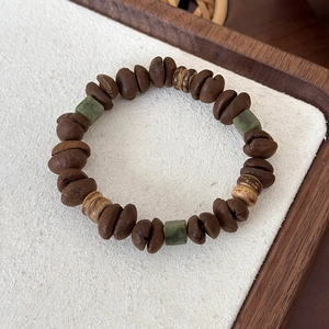 Close-up of coffee bean bead bracelet with green stones and wooden accents on white surface