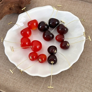 Realistic cherry dangle earrings in red and burgundy finishes on a ceramic plate