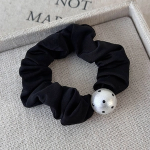 Detailed shot of a black pleated hair scrunchie with a vintage white polka dot bead