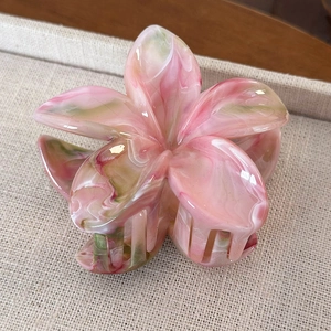 Dettaglio macro della molletta a fiore marmorizzata rosa su vassoio beige