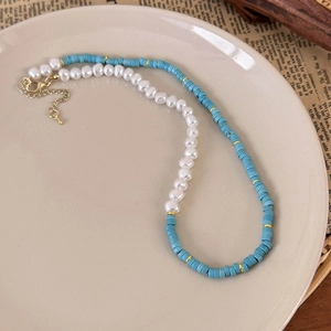 Close-up of pearl and green beaded necklace with gold metal clasp on a ceramic plate