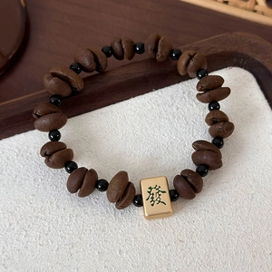 Close-up of coffee bean beads bracelet with a golden Mahjong charm showing Fa character