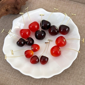 Detailed view of lifelike cherry earrings in vibrant red and dark purple on a white tray