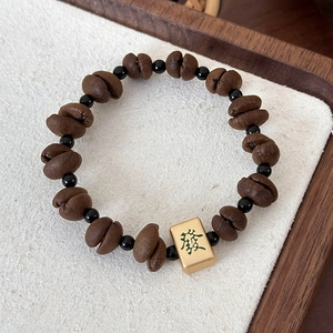 Detail of beaded coffee bean bracelet featuring black round beads and a golden mahjong charm