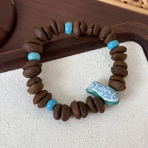 Detail of coffee bean beaded bracelet with turquoise accents and a ceramic fish charm