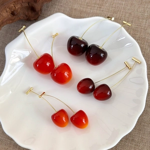 Detail of red and burgundy cherry earrings with golden posts on a ceramic shell tray