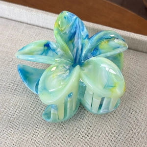 Dettaglio della molletta per capelli a fiore di frangipane con trama marmorizzata blu e gialla