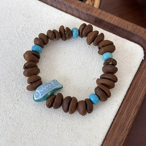 Detail of coffee bean beads and blue fish charm on an elastic cord bracelet
