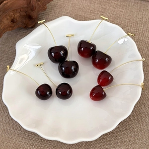 Deep red cherry drop earrings with gold stems displayed on a white ceramic plate