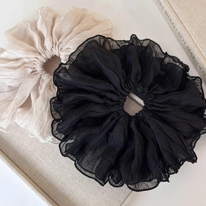 Detail of oversized pleated scrunchies in black and beige chiffon on a grey tray