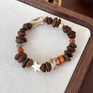 Detail of coffee bean bracelet with ceramic bone star and dog charms on wood tray