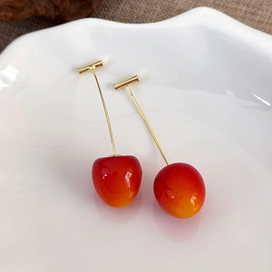 Macro detail of cherry earrings with red-orange gradient globes on white ceramic plate