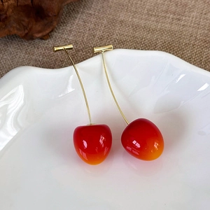 Macro detail of red gradient cherry earrings with gold stems on a white porcelain dish