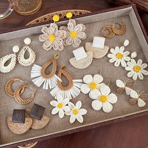 Bohemian woven raffia earrings in daisy and geometric styles on a linen display tray