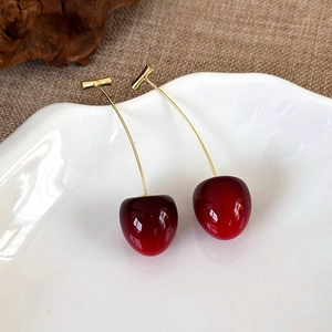 Close-up of translucent red cherry earrings with gold stems on a ceramic tray