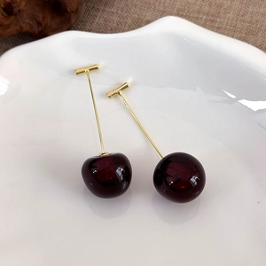 Detailed macro view of cherry-shaped drop earrings with deep red resin and golden metal stems
