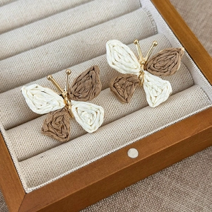 Macro detail of hand-woven butterfly earring with natural fiber and gold metal body