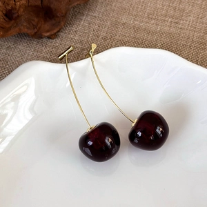 Close-up of dark red cherry earrings in a white ceramic tray with a natural aesthetic