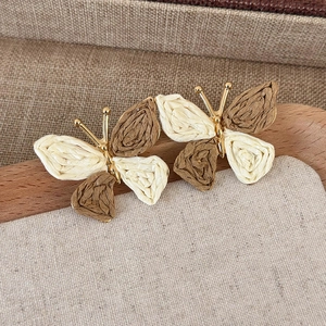 Detail of woven butterfly earrings featuring beige and brown raffia wings with gold accents