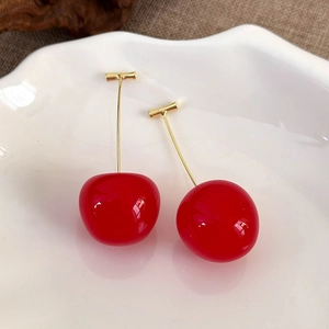Detail of red cherry earrings with high-gloss finish and gold-tone metal stems on white plate