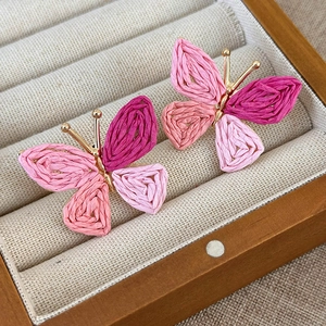 Detailed macro view of handmade pink woven butterfly earrings with gold metal frame